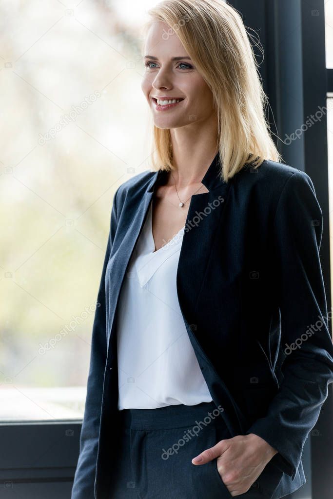 beautiful smiling blonde businesswoman standing with hand in pocket and looking away 