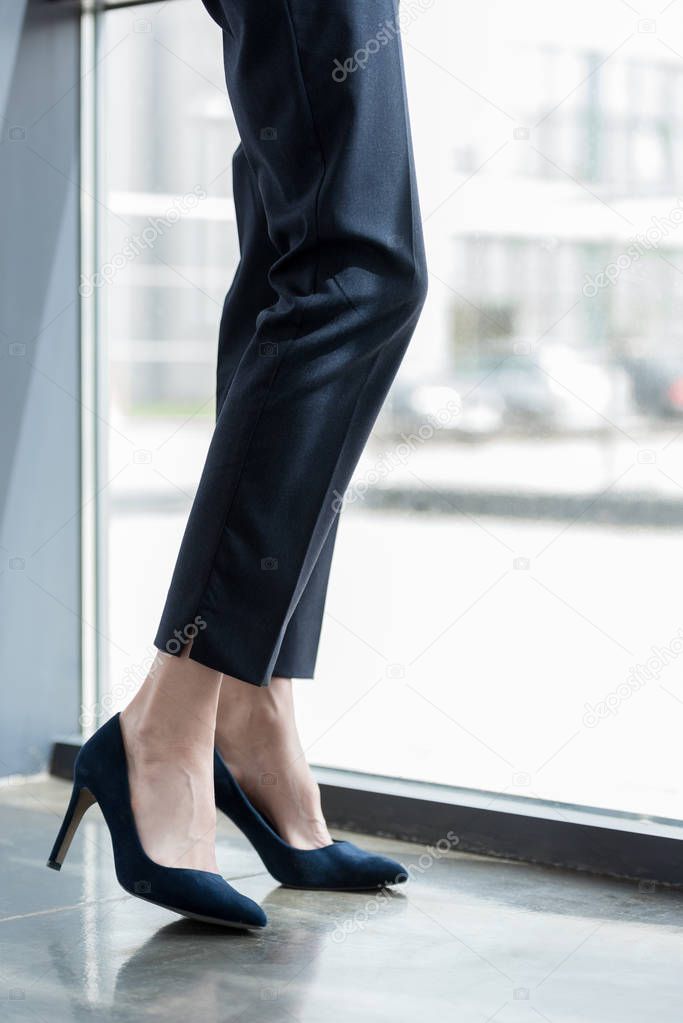 low section of businesswoman in high heeled shoes standing near window