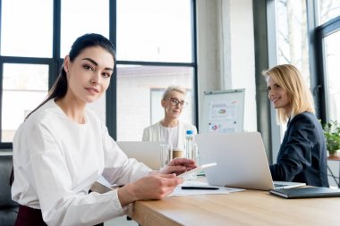 meslektaşları Office ile çalışırken kameraya gülümseyen genç iş kadını