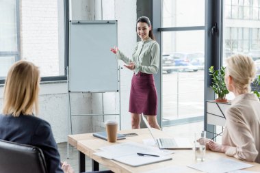 Flipchart üzerinde office toplantıda arkadaşları işaret eden iş kadını