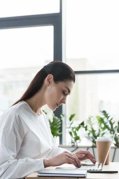 年轻女实业家在工作场所使用笔记本电脑的侧面视图 — 免费的图库照片