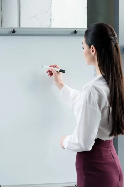 年轻女商人在空白白板上写字的侧面视图 — 图库照片