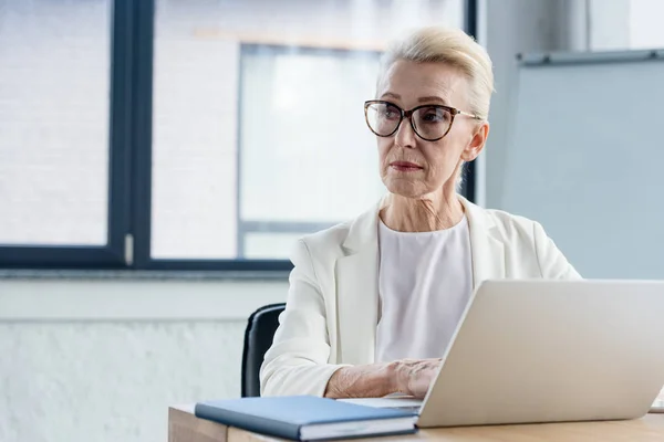 Serious Senior Businesswoman Eyeglasses Using Laptop Looking Away Office — Stock Photo, Image