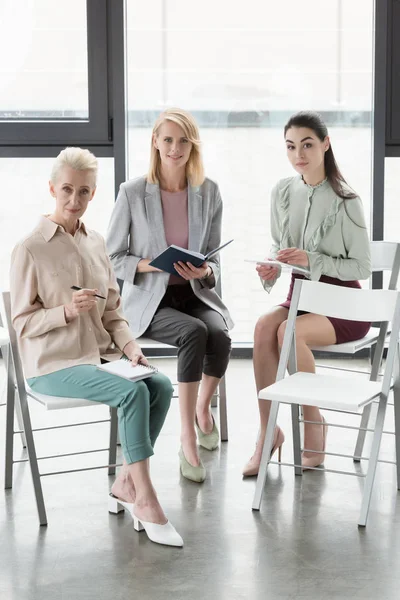 Schöne Geschäftsfrauen Die Auf Stühlen Sitzen Und Büro Die Kamera — kostenloses Stockfoto