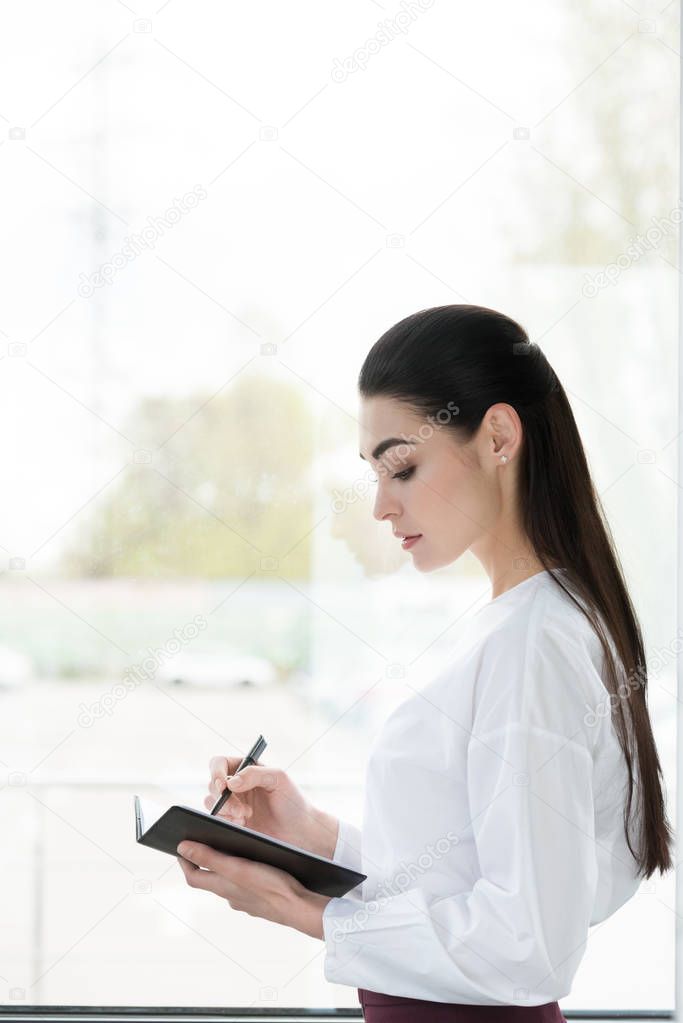 side view of beautiful young businesswoman taking notes in notepad