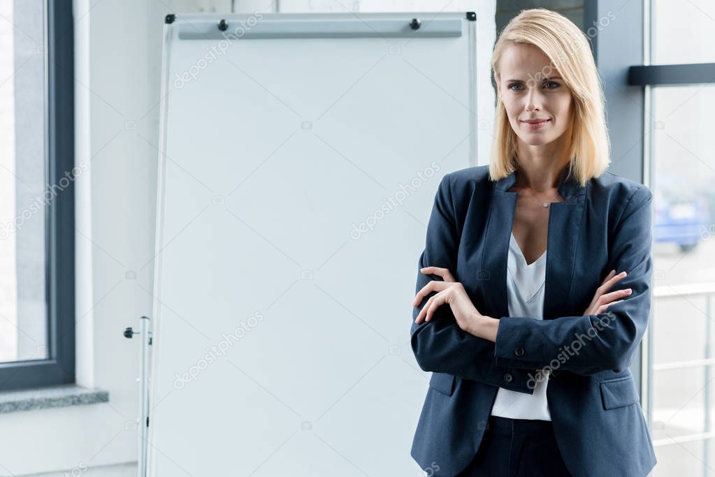 beautiful confident businesswoman standing with crossed arms and smiling at camera in office