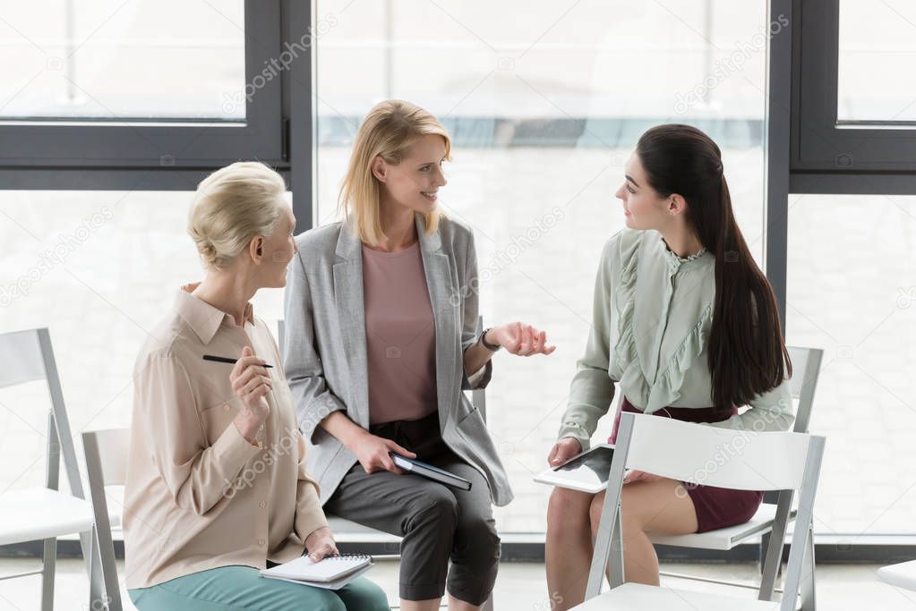 beautiful businesswomen sitting on chairs and talking in office