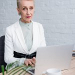 Caucasian senior businesswoman using laptop at workplace with coffee cup