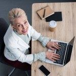 Bovenaanzicht van lachende senior zakenvrouw met behulp van laptop op werkplek