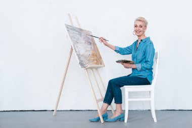 gülümseyen kıdemli kadın sanatçı atölye şövale üzerinde boyama