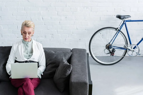 Senior Affärskvinna Med Laptop Soffan Office Med Cykel — Stockfoto