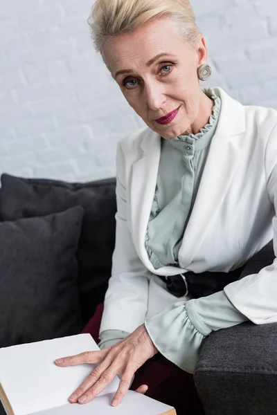Schöne Seniorin Liest Buch Während Sie Auf Dem Sofa Sitzt — kostenloses Stockfoto