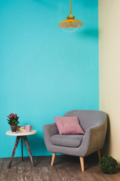 table with plant and armchair with pillow in room in vintage style