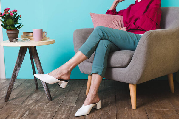 cropped view of elegant woman sitting in armchair with pillow