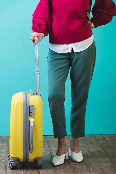 low section view of female traveler with yellow suitcase