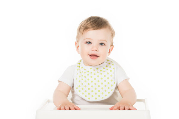 smiling baby boy in bib sitting in highchair isolated on white background 