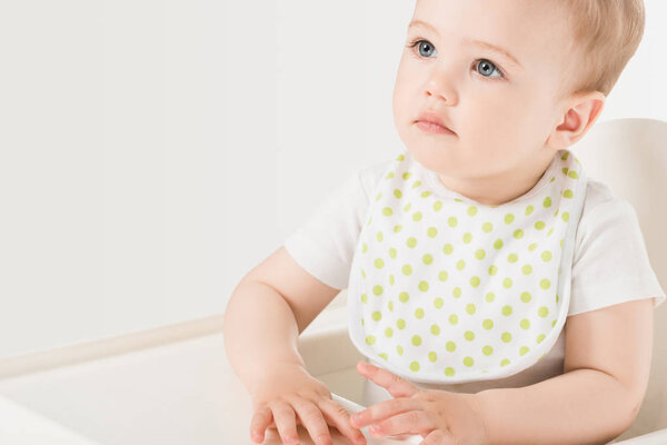 portrait of baby boy in bib sitting in highchair isolated on white background 