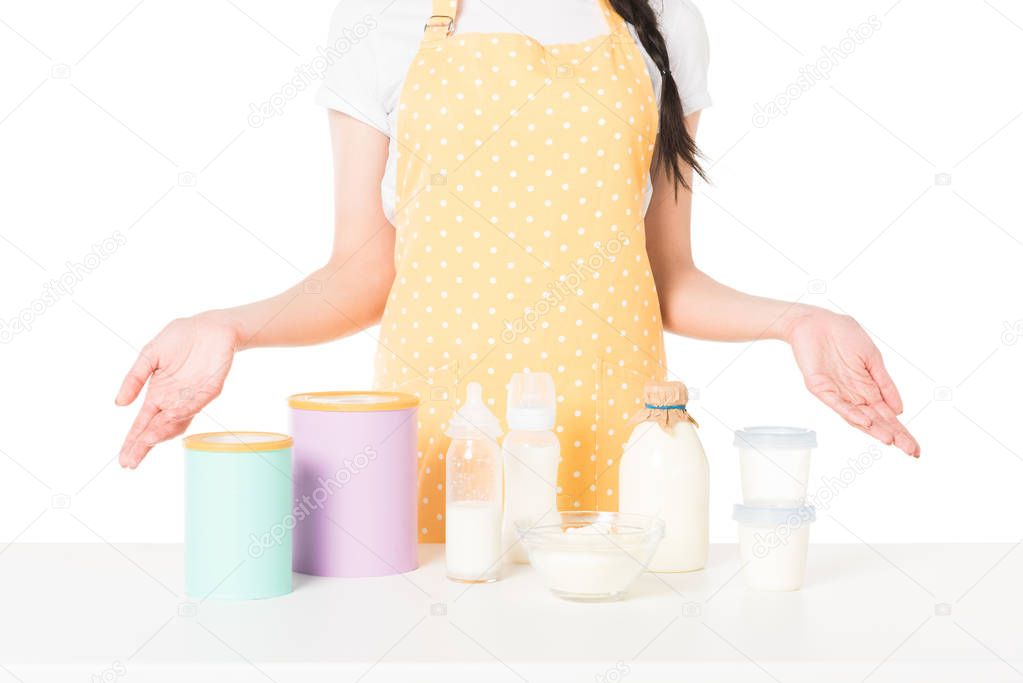 cropped shot of woman in apron with wide arms standing at table with children food and milk isolated on white background 