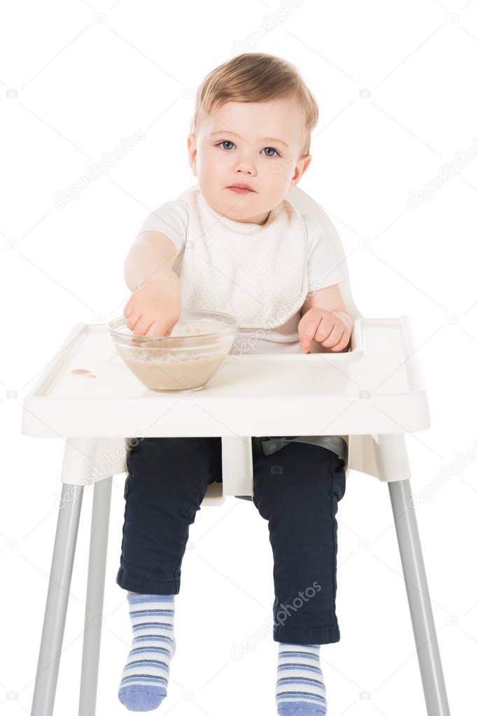 little boy in bib eating puree and sitting in highchair isolated on white background 