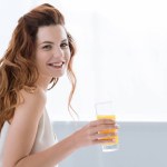 Smiling young woman with orange juice and pancakes with strawberry for breakfast looking at camera