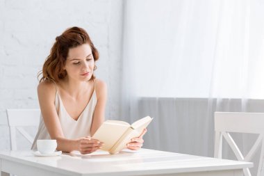 genç kadın masada evde kahve fincanı ile kitap okuma odaklı