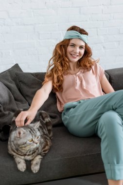 evde kanepede otururken gülümseyen genç kadın sevişme tekir kedi