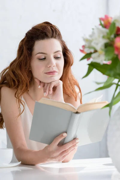 Attraktive Junge Frau Liest Buch Während Sie Mit Kaffeetasse Und — Stockfoto