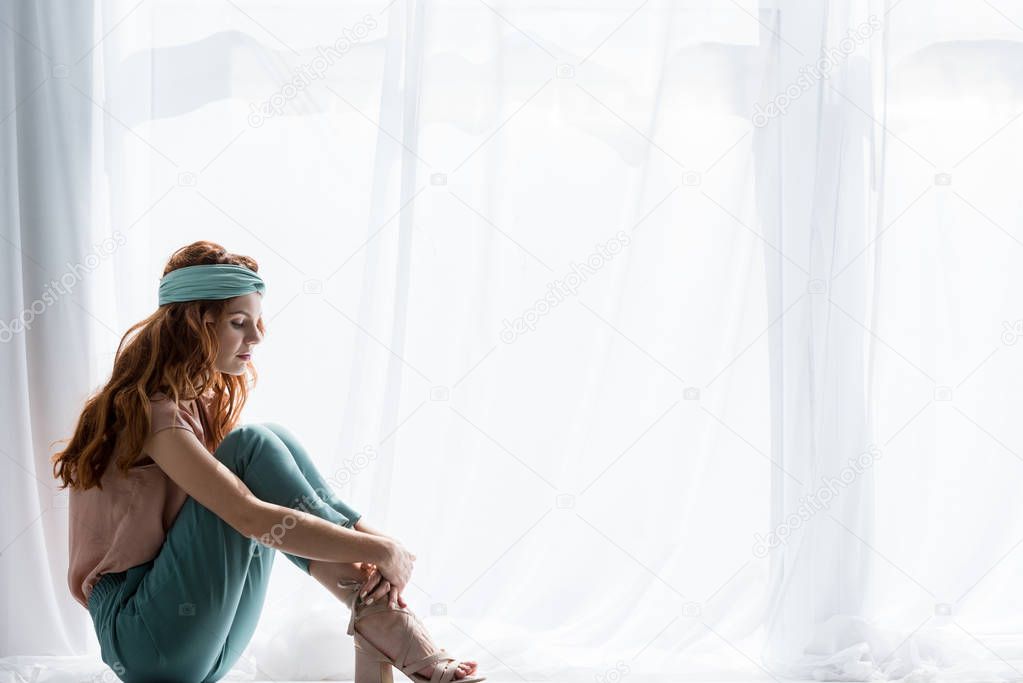 beautiful young woman sitting on windowsill alone