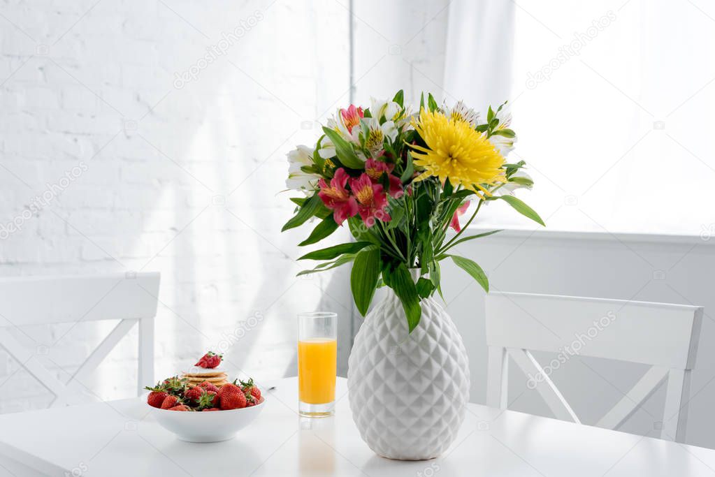 delicious pancakes with strawberries and flowers in vase on table