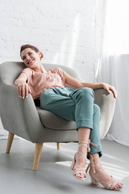 happy young woman relaxing on armchair at home clipart