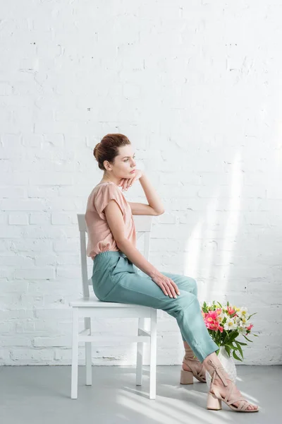 Thoughtful Young Woman Sitting Chair Flowers Floor Front White Brick — Stock Photo, Image