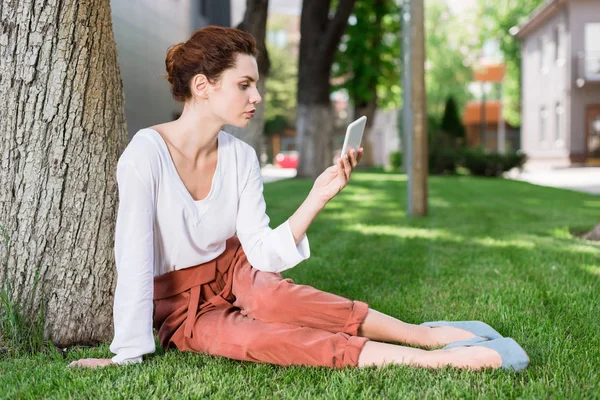 Atractiva Mujer Joven Usando Teléfono Inteligente Mientras Está Sentado Hierba —  Fotos de Stock