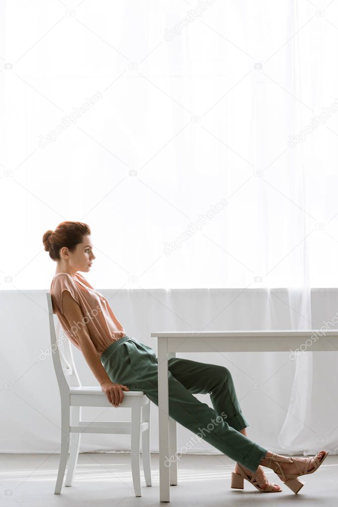 side view of beautiful young woman sitting at table at home