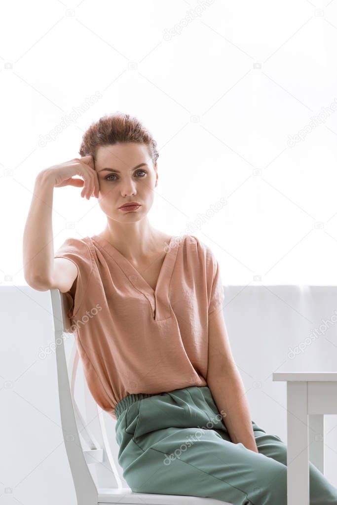 depressed young woman sitting on chair at home and looking at camera