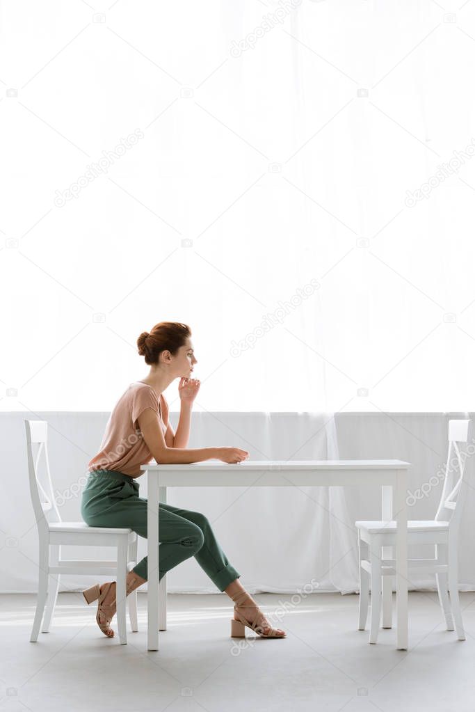 side view of beautiful young woman sitting at table alone at home