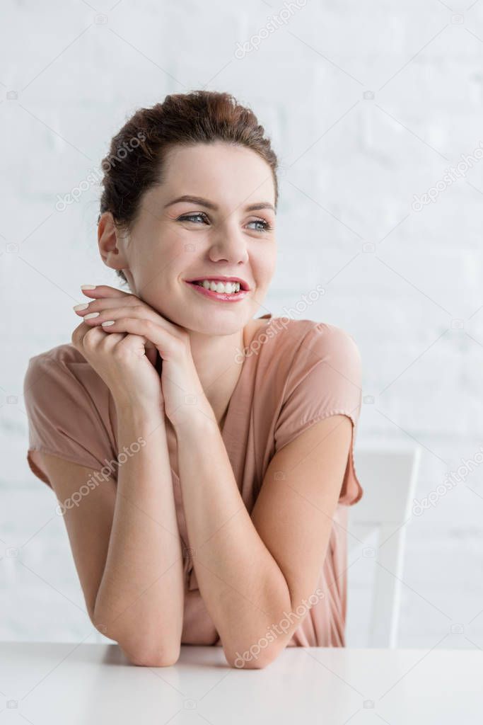 happy young woman sitting at table in front of white brick wall