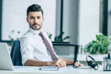 İş yerinde otururken kameraya bakan kendine güvenen iş adamı
