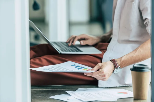 Cropped View Businessman Using Laptop Holding Paper Infographics While Sitting — Stock Photo, Image