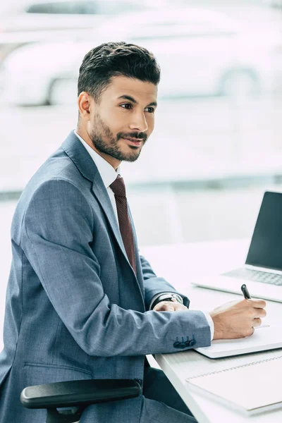 Sonriente Hombre Negocios Escribiendo Cuaderno Mirando Hacia Otro Lado Mientras — Foto de Stock