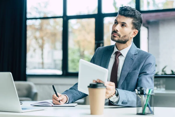 selective focus of thoughtful businessman looking away while holding digital tablet and pen