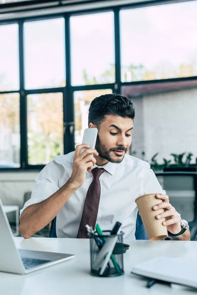 Hombre Negocios Positivo Mirando Taza Desechable Mientras Habla Teléfono Inteligente — Foto de Stock