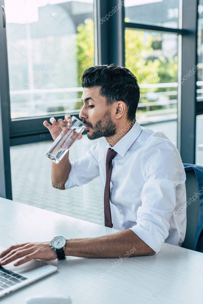 thirsty businessman drinking water while using laptop