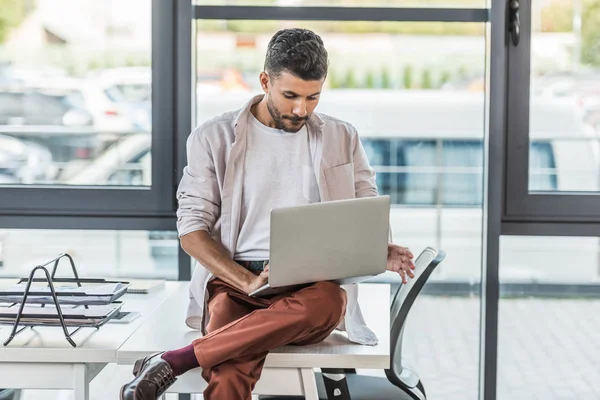 若いビジネスマンが机の上に座ってノートパソコンを使って — ストック写真