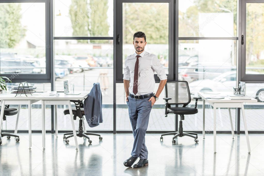 young, confident businessman standing in modern office and looking at camera 