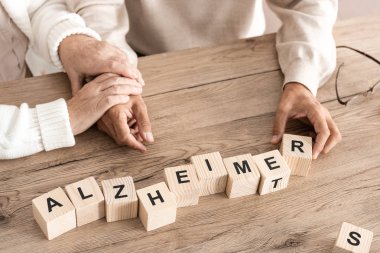 Tahta küplerin yanında Alzheimer harfleriyle oturan emekli çiftin görüntüsü. 