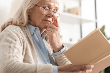 Alzheimer hastası yaşlı bir kadının seçici odak noktası insan parmağı hatırlatıcı kitap okuması. 