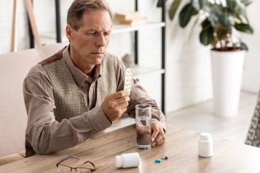 Alzheimer hastası emekli bir adamın seçici odak noktası. Elinde haplar ve bir bardak su var. 