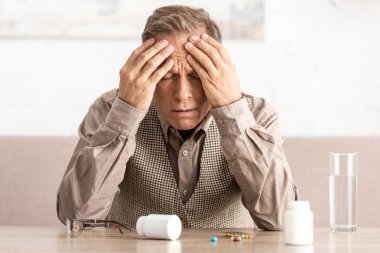 Alzheimer hastası hasta emekli bir adam. Masadaki ilaç ve şişelerin yanında. 