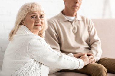 Alzheimer hastası bir kocanın elini tutan üzgün, emekli kadının seçici odağı. 