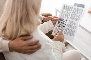 cropped view of senior man hugging wife with pencil and crossword  clipart